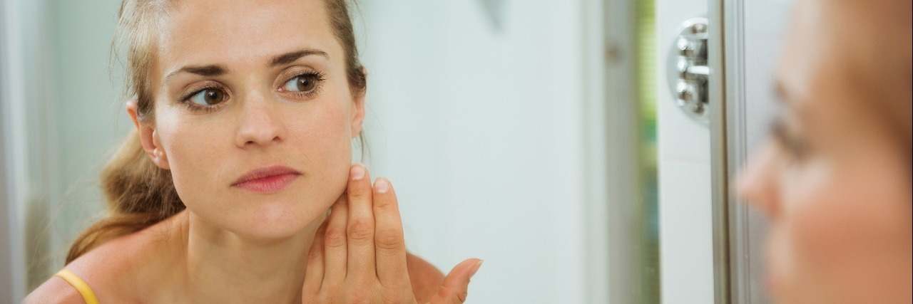 young woman checking her face in bathroom mirror