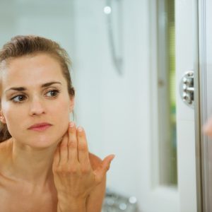 young woman checking her face in bathroom mirror