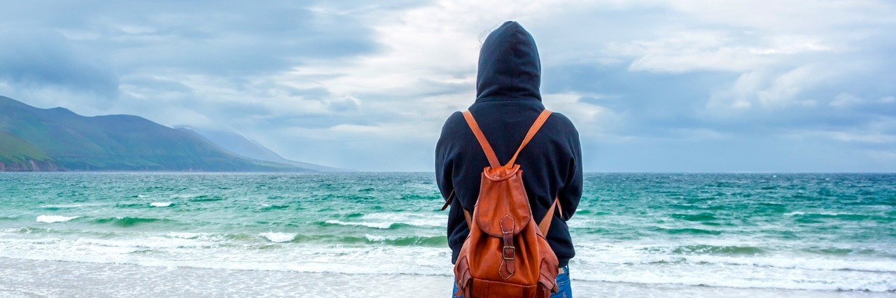 Coping With Grief and Remembering Significant Dates Person wearing hoodie and backpack, standing in front of ocean on cloudy day