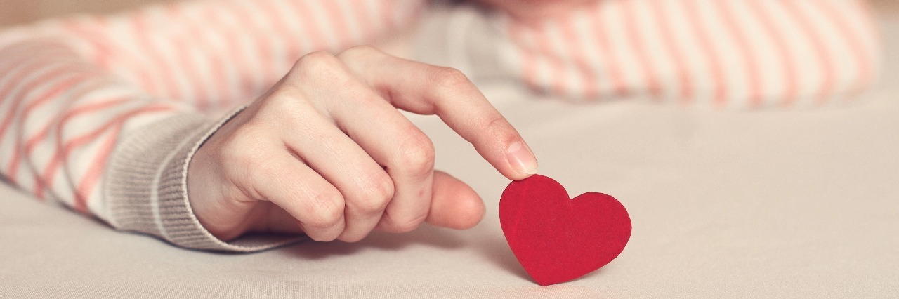 Why I'm Scared My Mental Illness Makes Me Hard to Love sad girl holding heart by tip of finger on table
