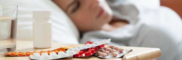 medication on night table in bedroom beside unwell looking woman
