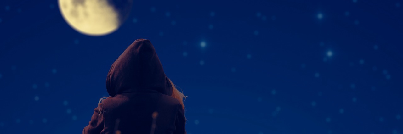 girl in a hoodie sitting outside at night and looking at the moon
