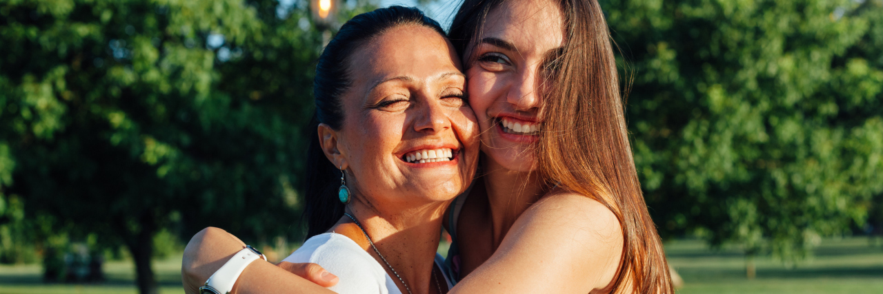 Cute pretty teen daughter with mature mother laughing and hugging in nature at sunset
