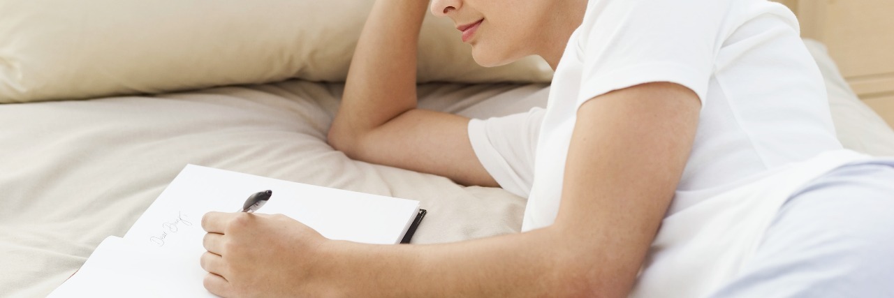young woman lying on bed writing in notebook