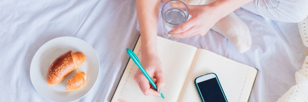 How Keeping a Diary Helps Me Manage My Chronic Illness Woman sitting on a bed, journaling.