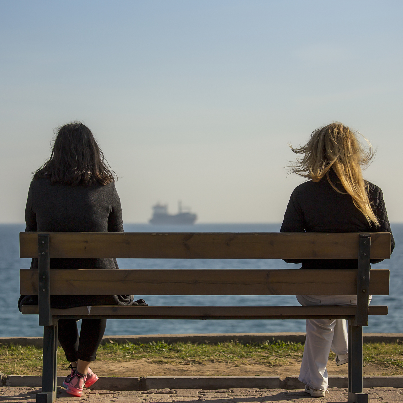 two women sit bench near beach