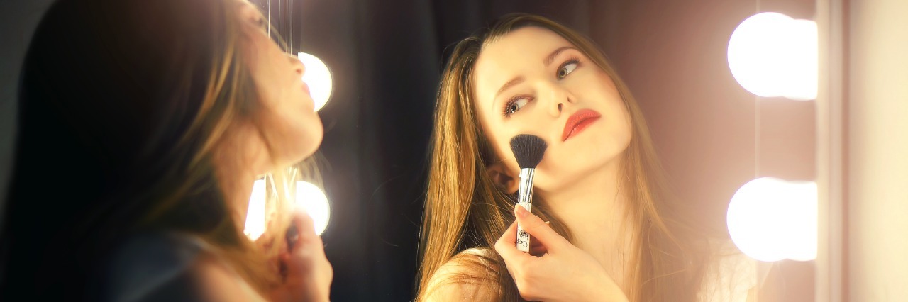 The Responses I Receive After Telling People I Have Fibromyalgia Young woman looking into mirror, putting on blush.