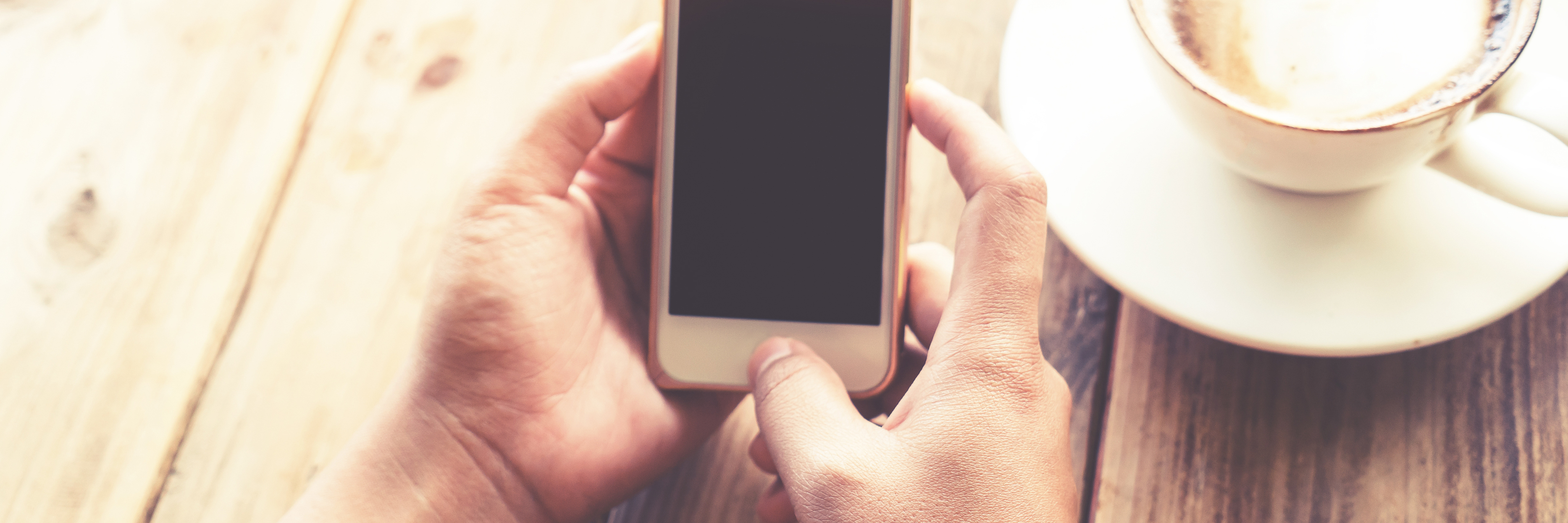 12 iOS and iPhone Apps for Emotional Wellness close up of woman's hands in coffee shop holding smartphone near coffee cup on wooden table. vintage light filter