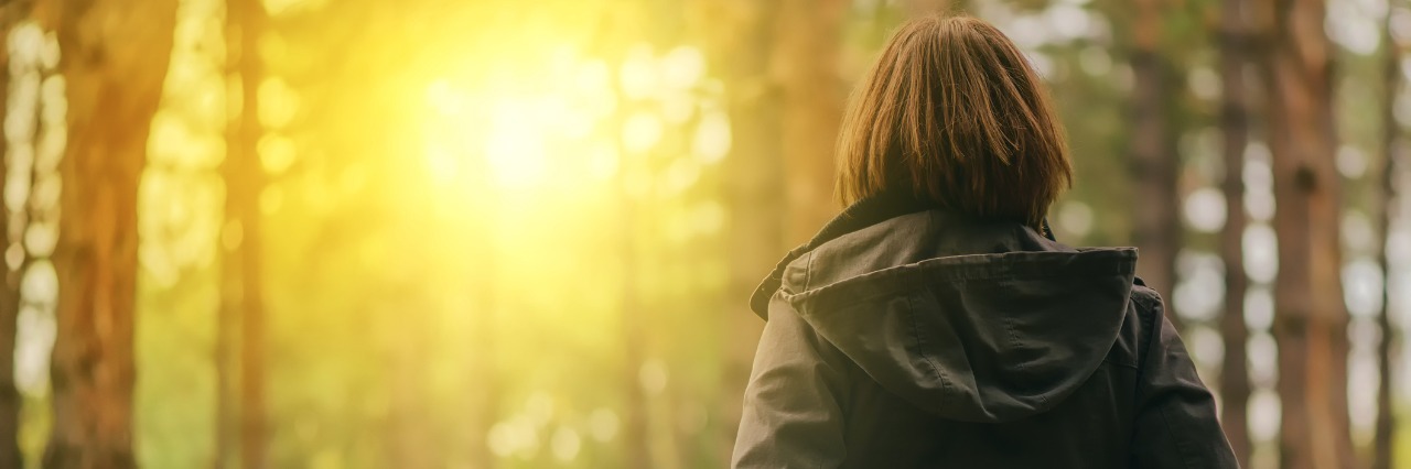 Accomplishing Goals with Chronic Illness and Pain woman looking at sunlight shining through trees