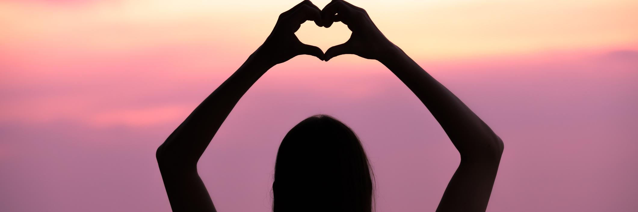 Woman making a hand shaped heart at sunset.