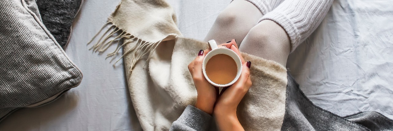 young woman sitting on bed holding a cup of coffee