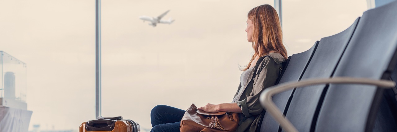 IBD: What to Know Before Moving Abroad With Chronic Illness woman sitting at the airport with her luggage waiting to catch a plane