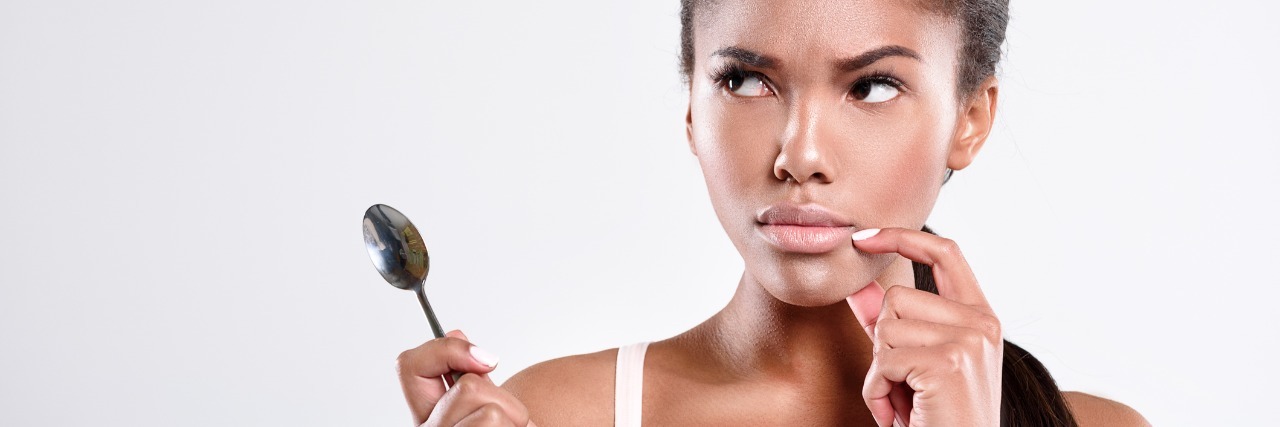 A woman with a serious facial expression, while holding a spoon in the air.