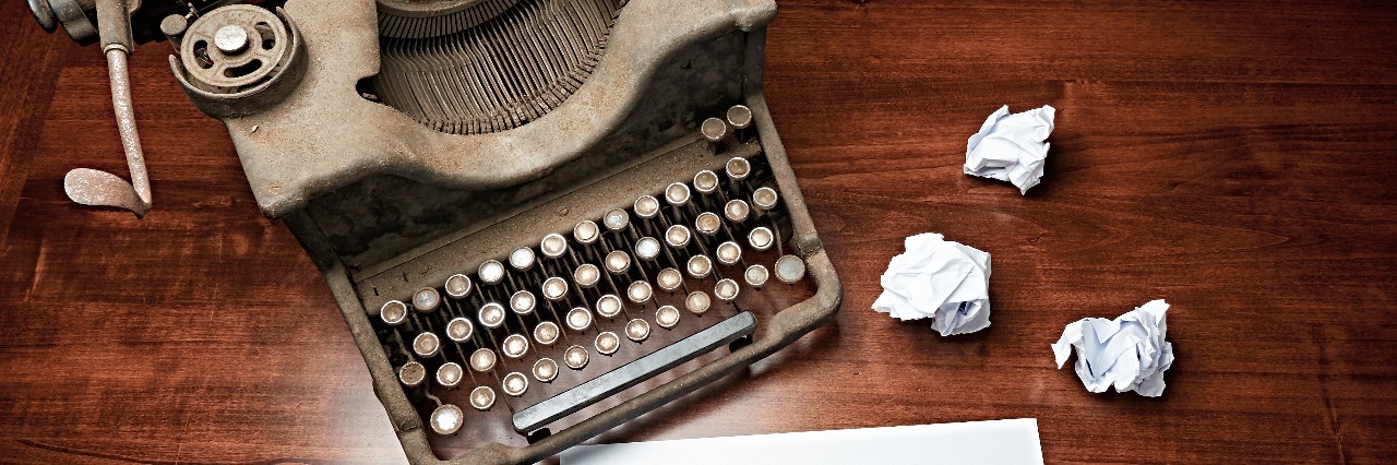 Chronic Pain: A Story With No End A typer writer with paper nearby, some paper also wadded up in balls next to pile of paper.