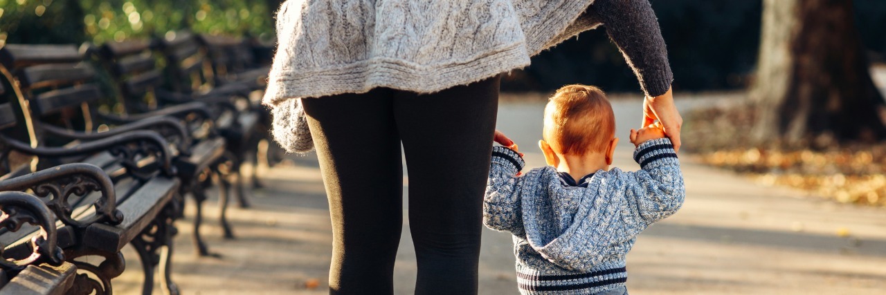 woman helping toddler walk in park