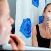 girl shaving face in bathroom mirror