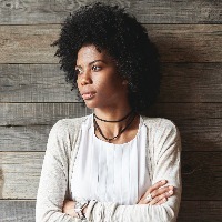 African American woman standing in front of a wooden panel wall, arms crossed.