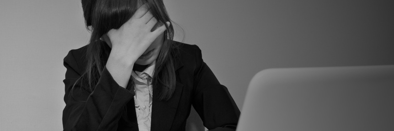 Stressed or headache businesswoman at office desk - black and white business concept