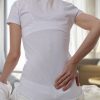 woman sitting on her bed and holding her back in pain