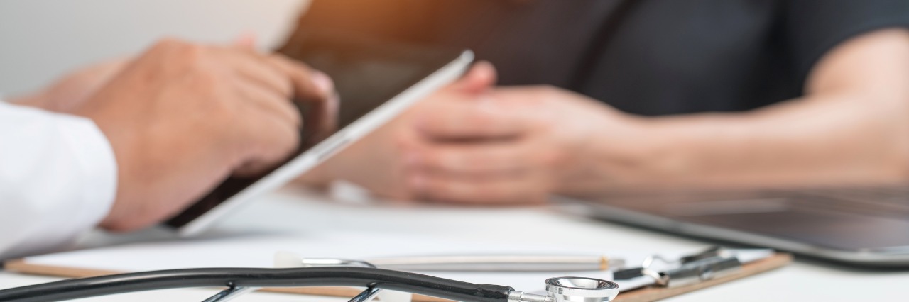 Doctor Telling Patient With Chronic Illness 'It's All in Your Head' doctor typing on tablet while talking to female patient