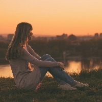 woman sitting on a hill overlooking a city during sunset