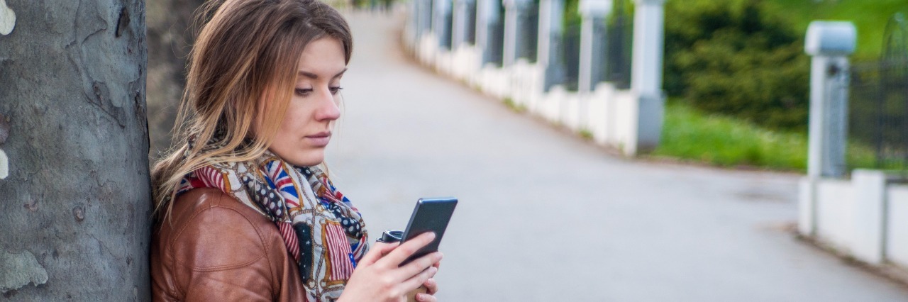 Please Don't Tell Me How to 'Cure' My Health Young woman on her phone, unhappy and tired looking.