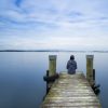 woman sitting on wooden pier on still lake