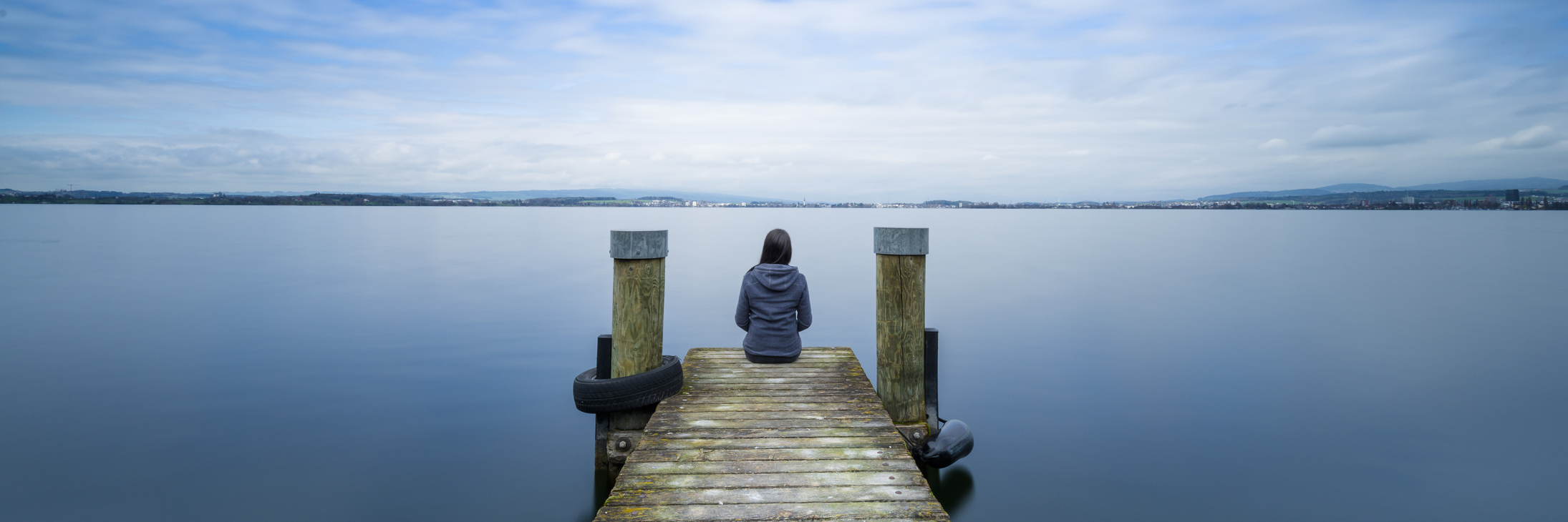 Finding Motivation to Make a Change for Your Mental Health woman sitting on wooden pier on still lake