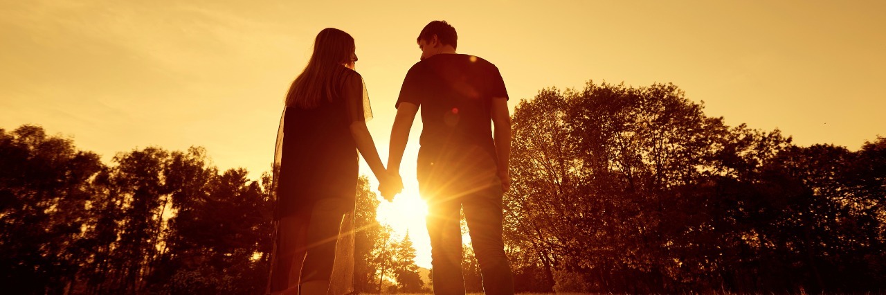 Fibromyalgia: Loving Your Partner Who Takes Care of You While Sick a couple handing hands at a park during sunset