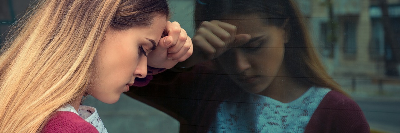 My First Day at My New Job While Battling Anxiety closeup of young business woman with head on window and reflection unhappy