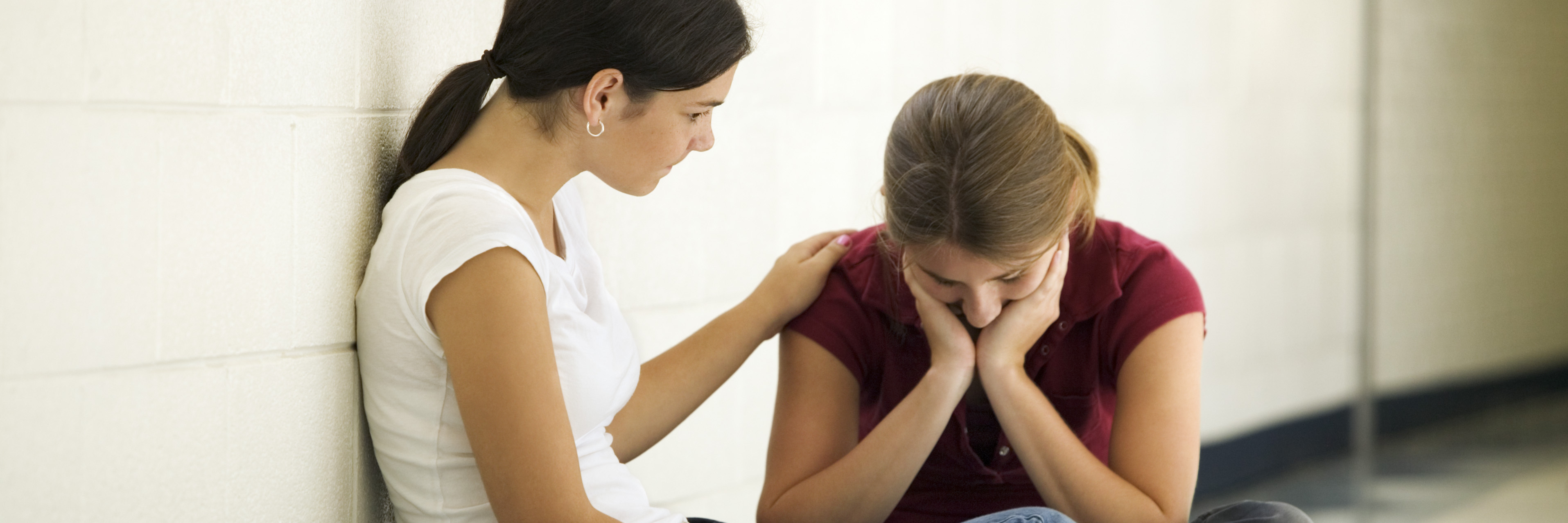 Ways to Help Someone Who Is Thinking About Suicide two young women sitting on floor in hallway with one offering support to the other