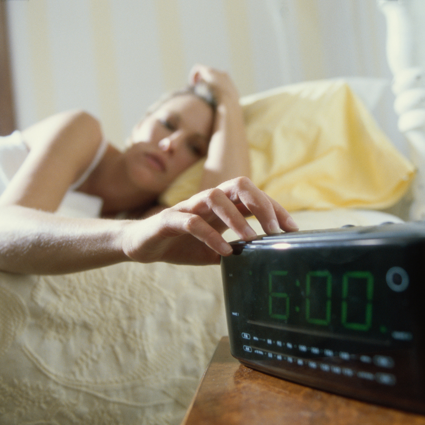 woman lying in bed and reaching for her alarm clock