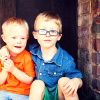 Twin boys with blonde hair. One wears glasses and the other has Down syndrome.