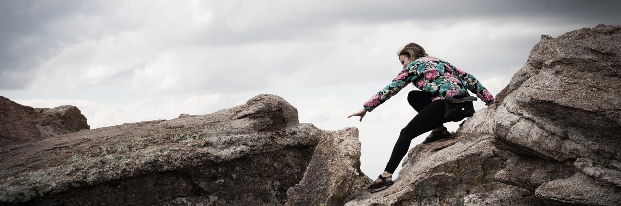 woman atop a rock with stormy clouds overhead as she reaches for the next one