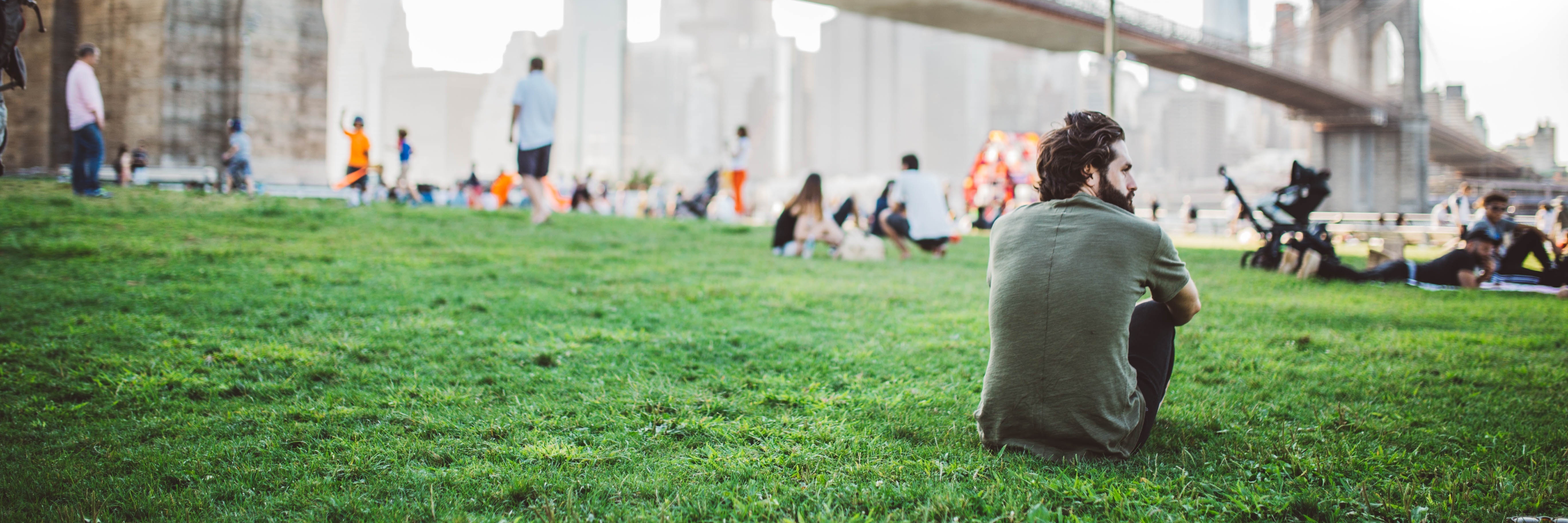 How to Manage Panic and Anxiety During Political Turmoil contemplative man sitting on grass near bridge in booklyn new york