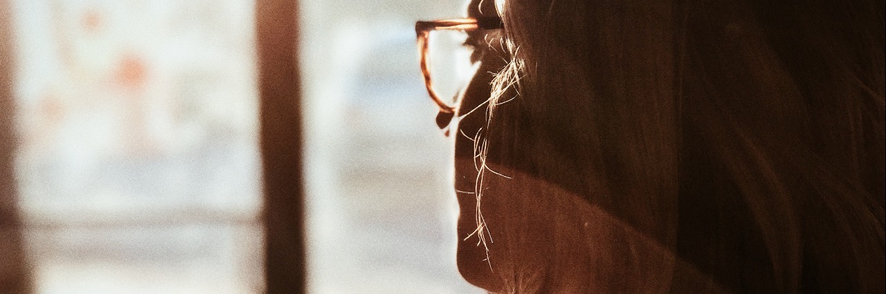 young woman wearing glasses with long light hair looking at sunlight through doorway