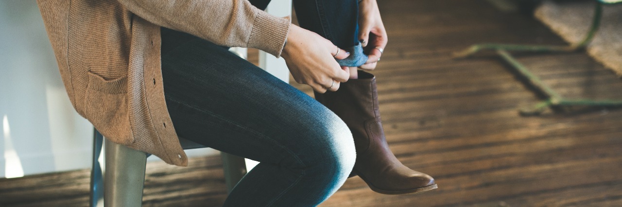 With a Mental Illness, My Hard Work Comes From Unexpected Places woman putting on boots and sitting on a stool