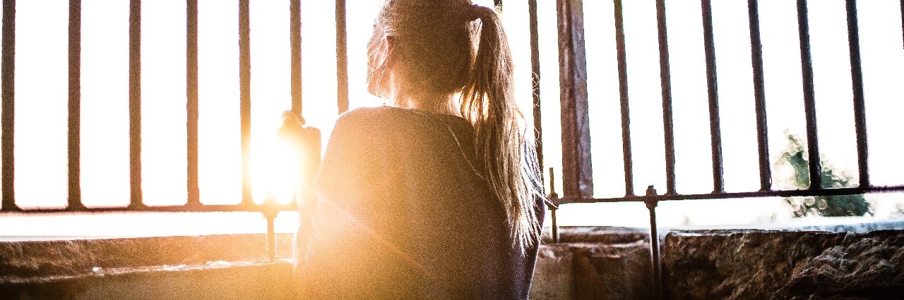 young woman standing in sunlight surrounded by bars