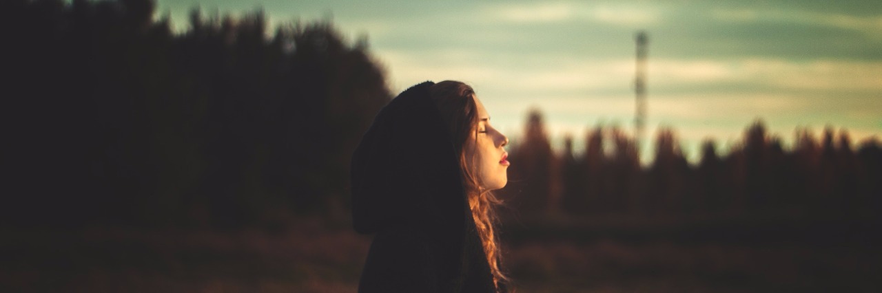 Why Your Past Does Not Define You or Make You Foolish young woman standing in field near forest at sunset with eyes closed