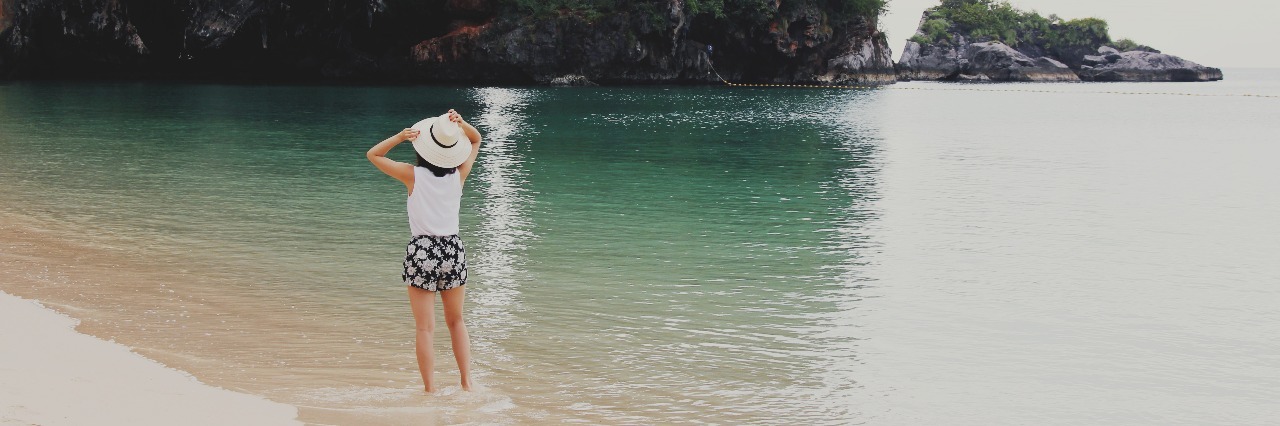 woman standing in ocean on idyllic beach with rock formation in distance