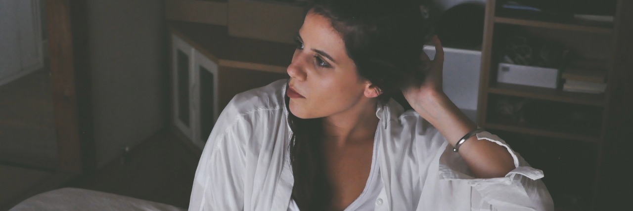 Why the Secrecy and Skepticism Around Mental Health Is Dangerous woman with dark hair sitting on bed looking away from camera