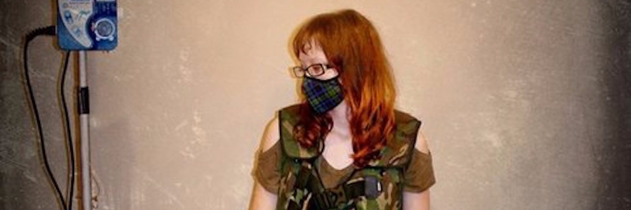 Constantly Battling Cystic Fibrosis woman sitting on the floor with a mask over her mouth and pill bottles in front of her