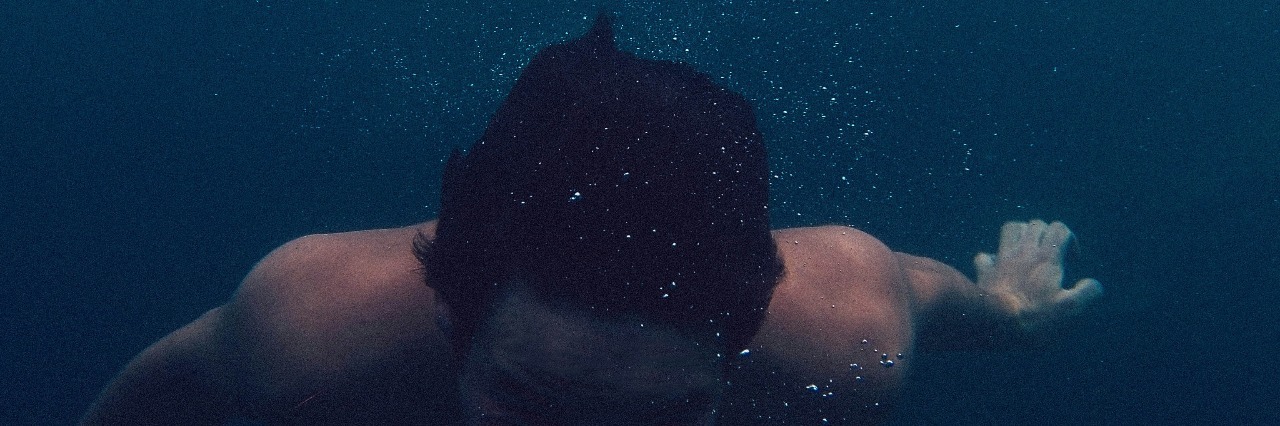 topless man with dark hair in ocean, face hidden