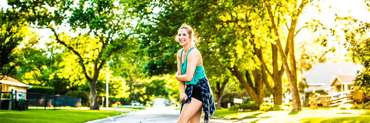 young woman standing in middle of sunlit street laughing