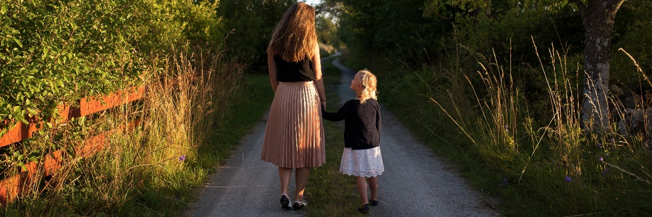 What I Will Tell My Future Children If They Inherit My Mental Illness mother and daughter walking hand in hand down beautiful country lane while daughter looks up at mother