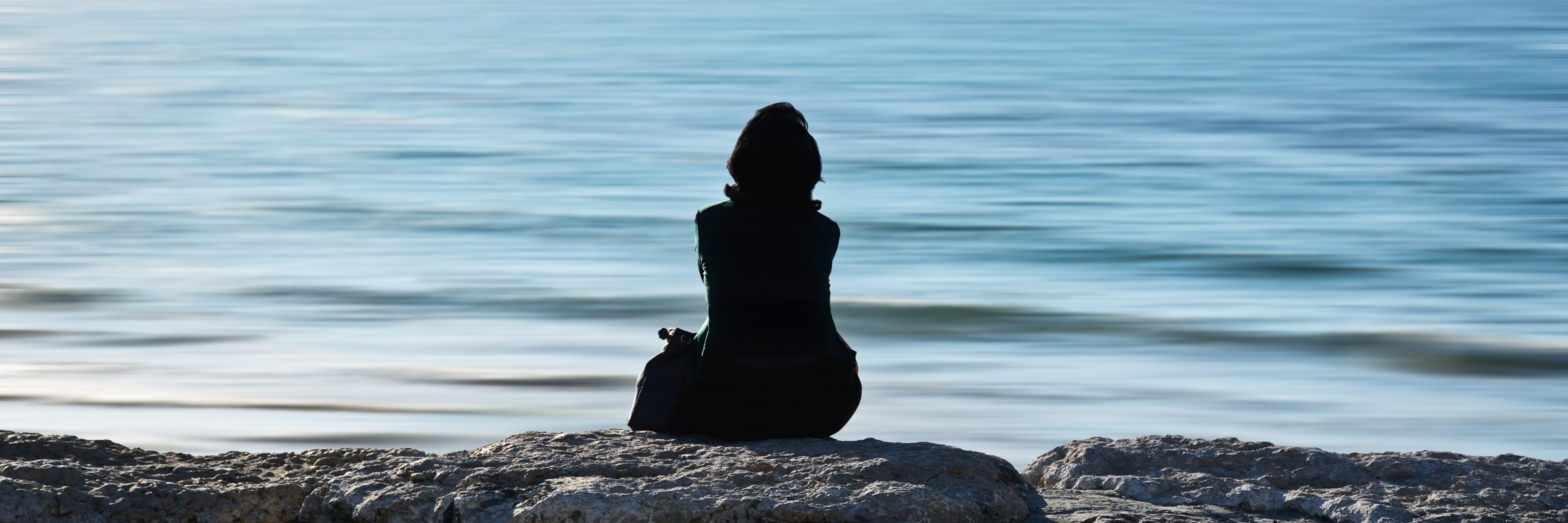Why Loneliness Is the Worst Part of Having Anxiety woman sitting alone in front of ocean with seagull in distance