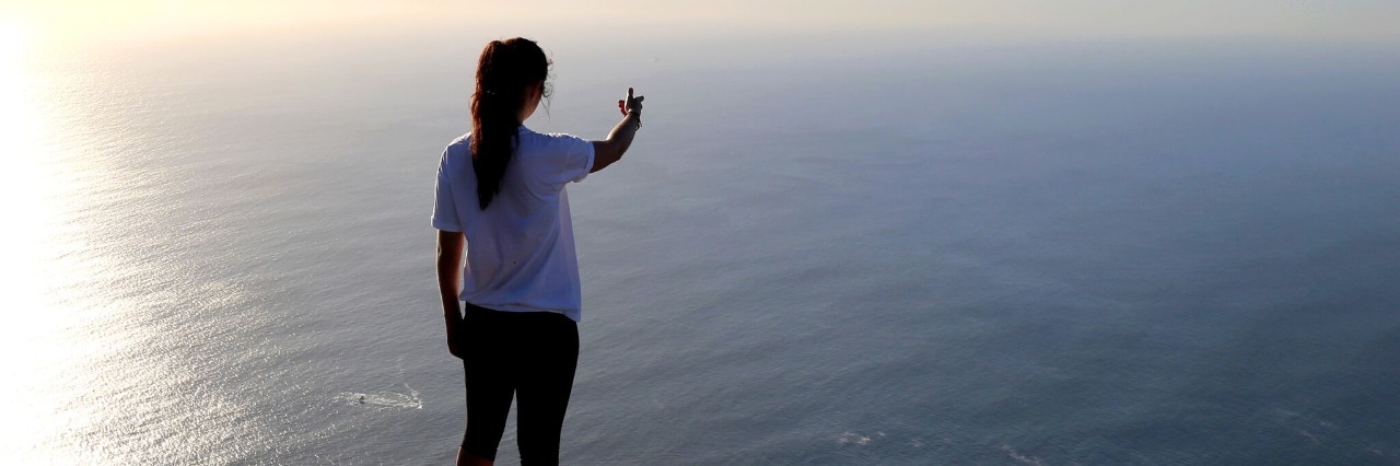 Wanting Positive Test Results When You're Undiagnosed woman standing on a cliff overlooking the ocean