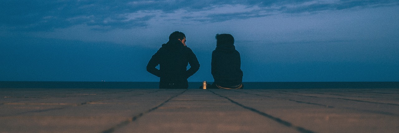 How Can You Help Someone With a Mental Health Issue? two people sitting on edge of pier or platform with dark clouds in distance and drink can between them