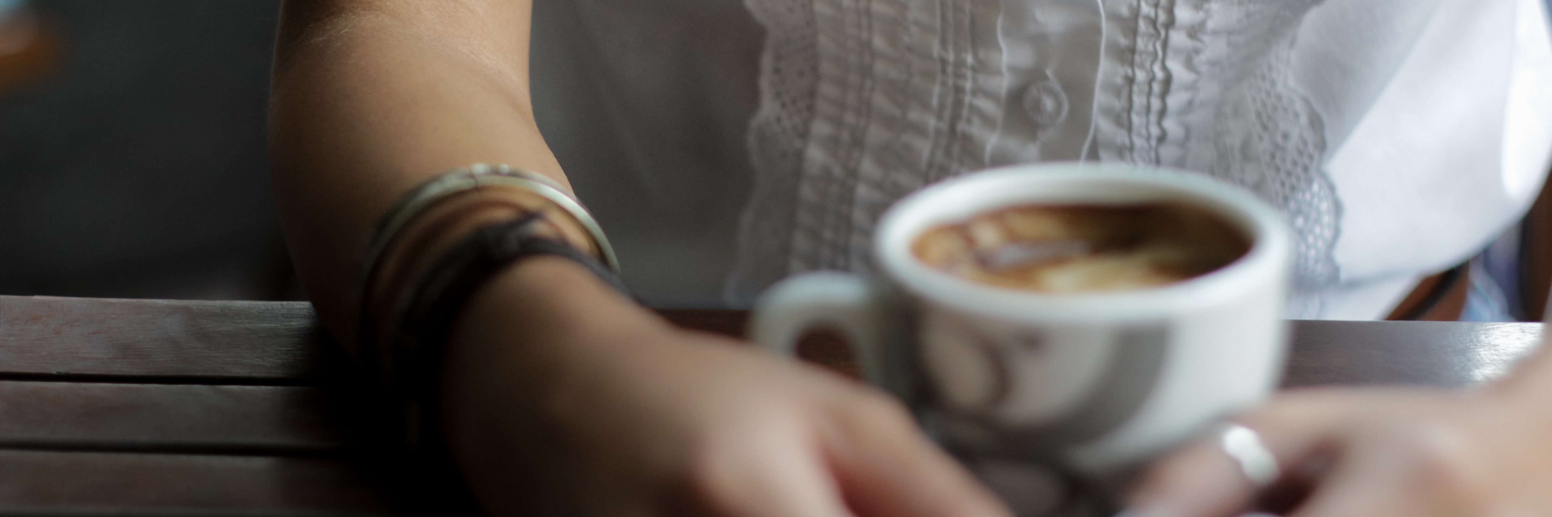 woman with arm tattoo sitting with coffee at wooden table