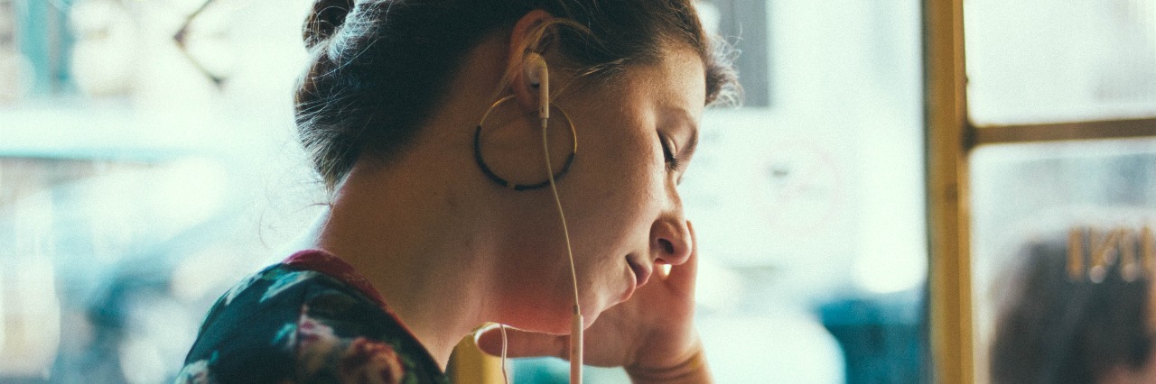 young woman in public space listening to music on earphones